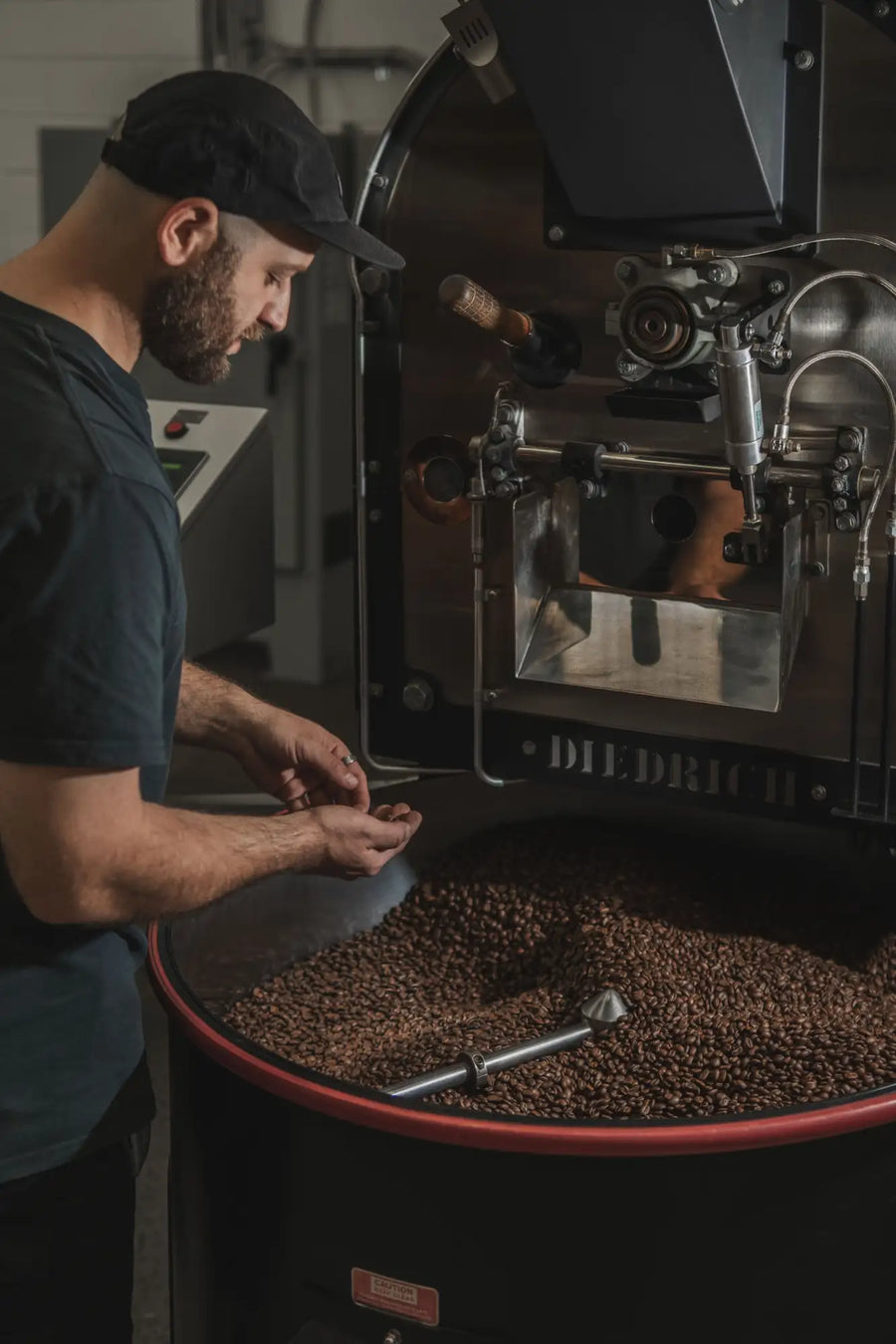 Black and red industrial coffee roaster with stainless steel interior and visible branding on the side