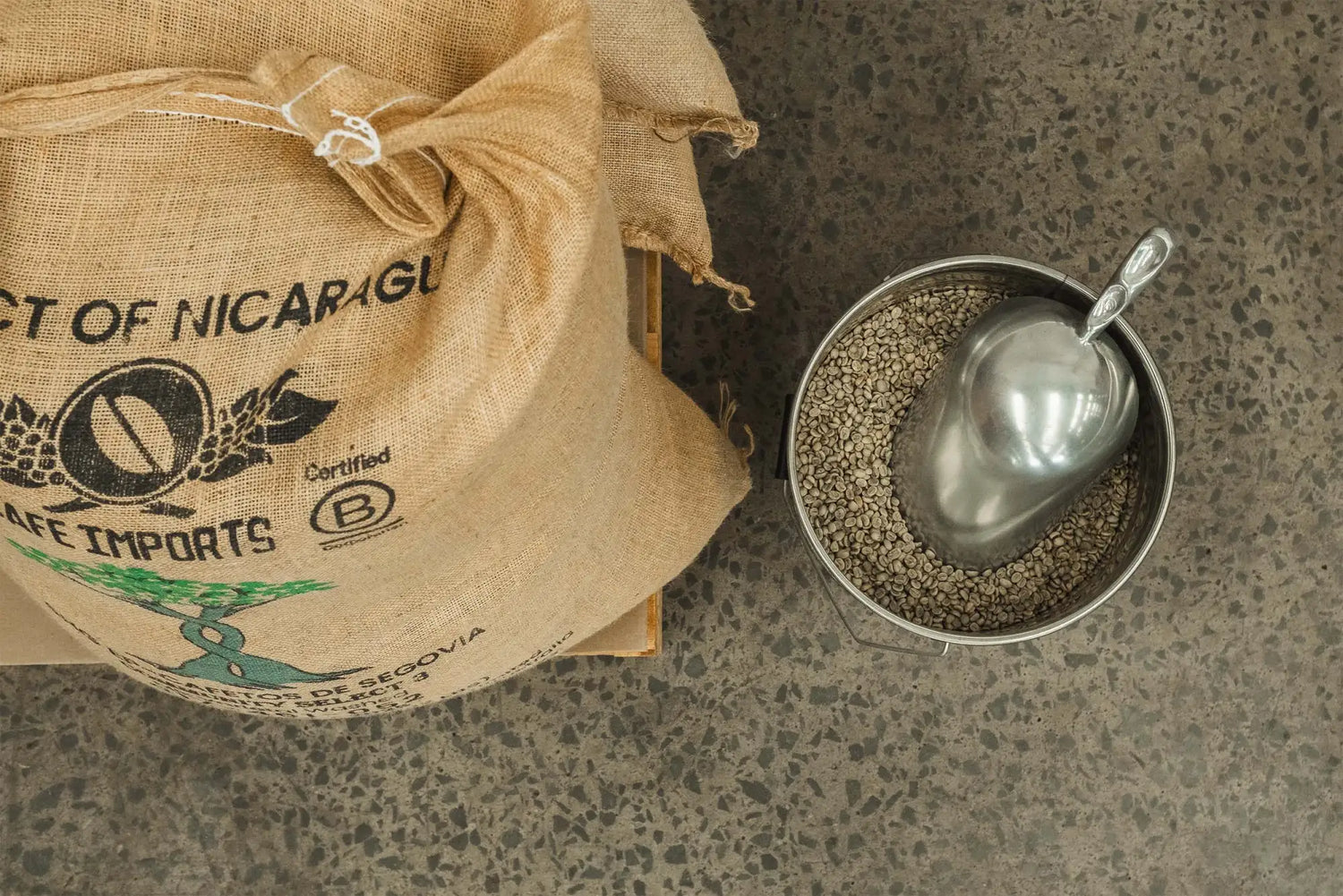 A burlap sack labeled ’coffee imports’ with a green tree logo, containing coffee beans.