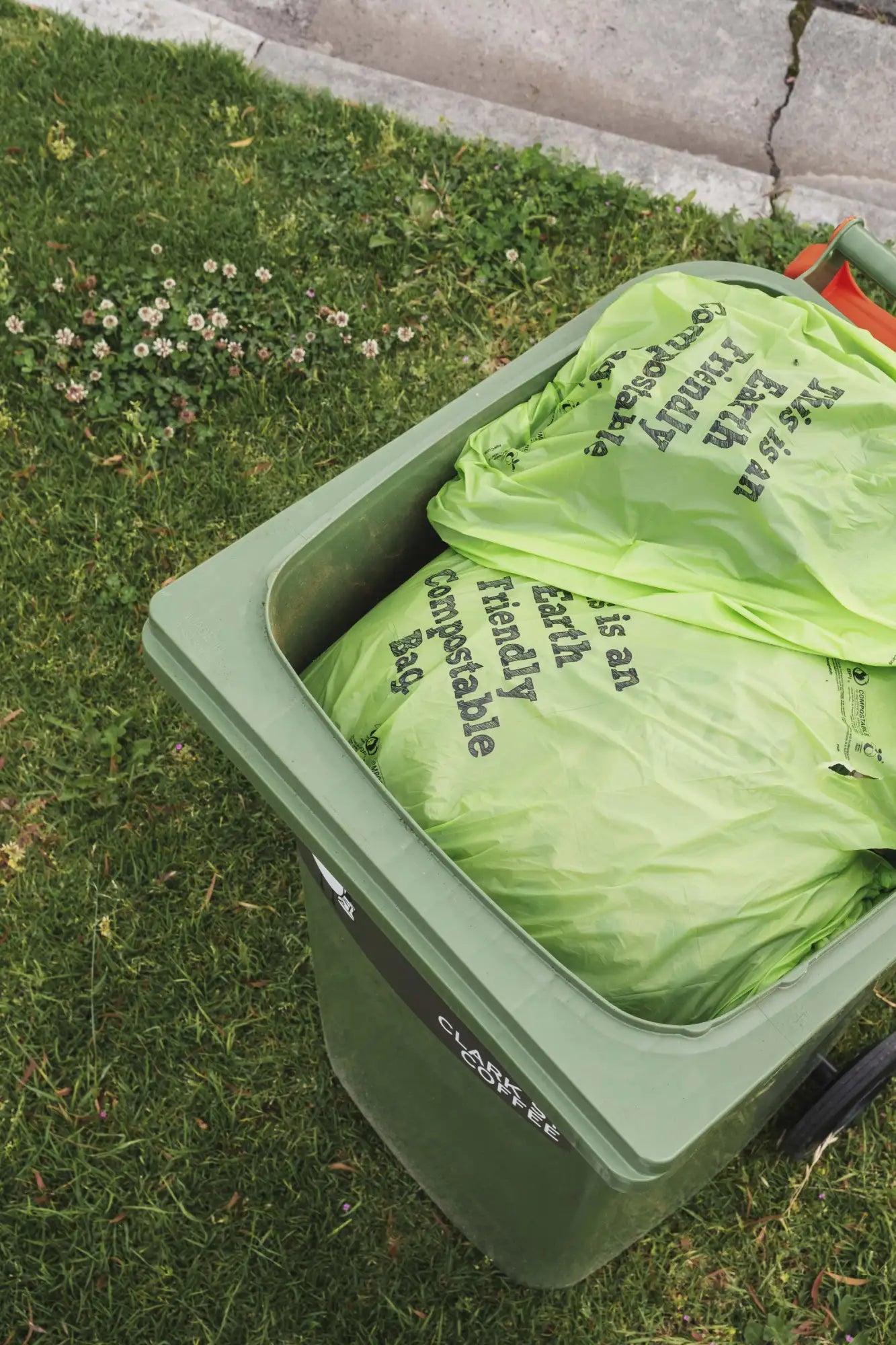 Green plastic recycling bin filled with lime green compostable bags.