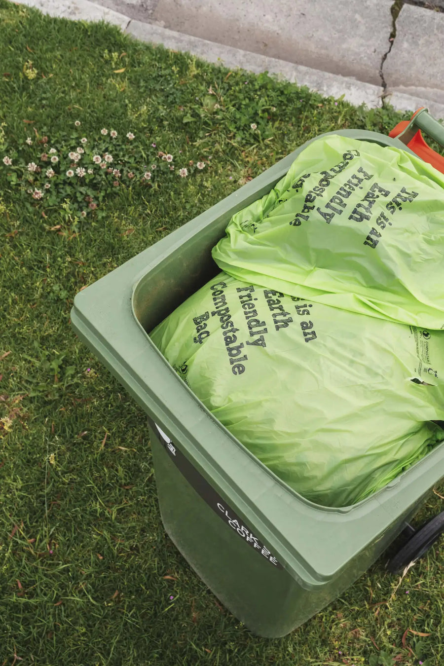 Green plastic recycling bin filled with lime green compostable bags.