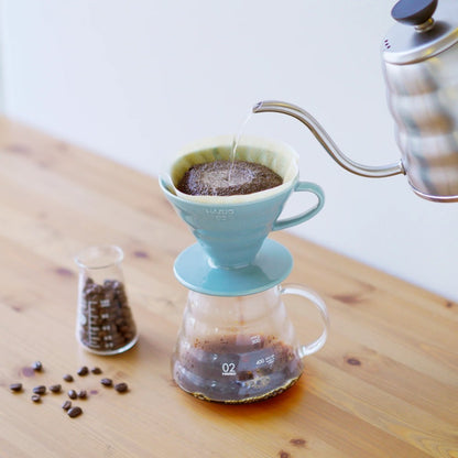 Pouring hot water from a gooseneck kettle into a light blue Hario V60 ceramic dripper on a glass server