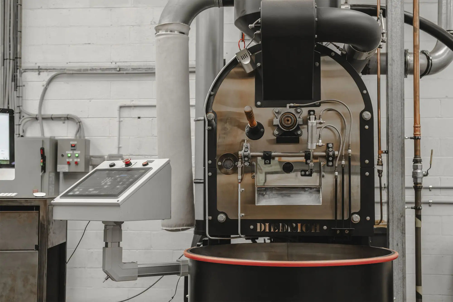 Industrial-grade coffee roaster with a stainless steel body, black accents and red trim around the base.